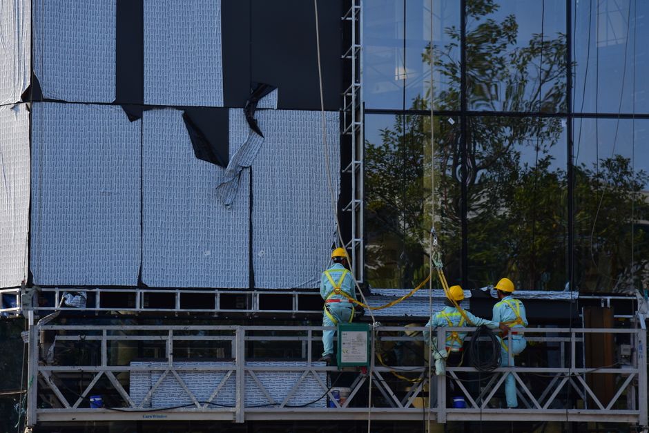 A team of construction workers in safety gear repairing a building facade using scaffolding.